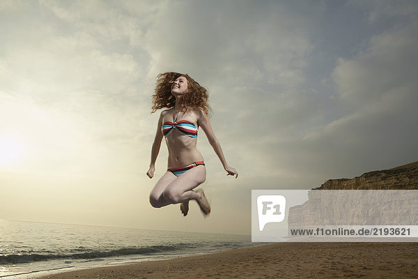 Frau springt mit Strandhintergrund.