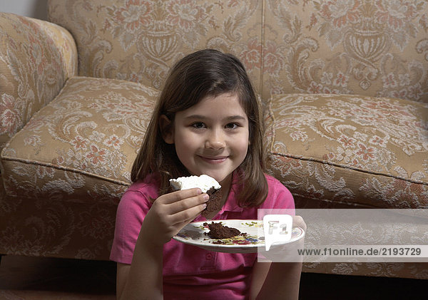 Mädchen (6-8) am Sofa sitzend  Kuchen essend  lächelnd  Portrait