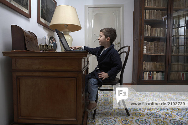 Junge (4-6) sitzend am Schreibtisch mit Laptop