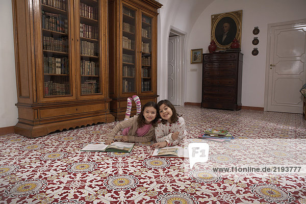 Girls (6-11) lying on floor reading books  smiling  portrait
