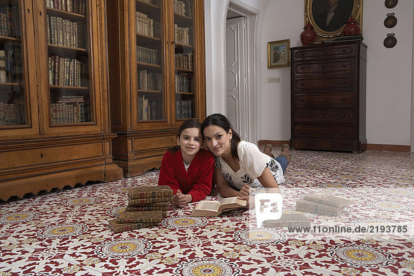 Mother and daughter (5-7) lying on floor reading books  portrait