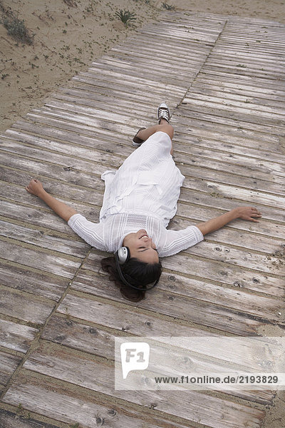 Woman wearing headphones lying on boardwalk