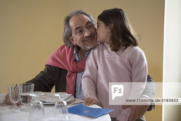 Mädchen (6-8) küssend Großvater am Esstisch