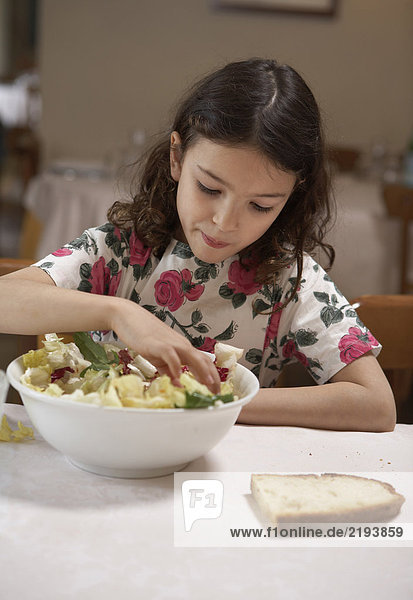 Girl (5-7) eating salad from bowl at a table