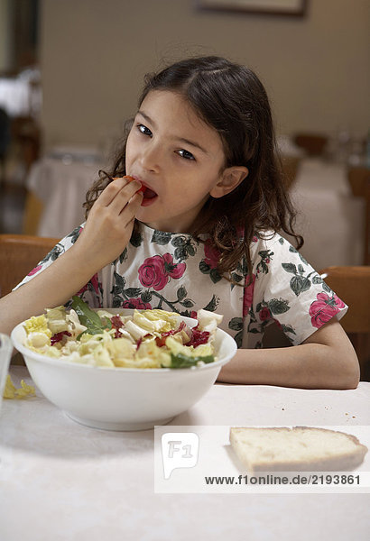 Girl (5-7) eating salad from bowl at a table  portrait