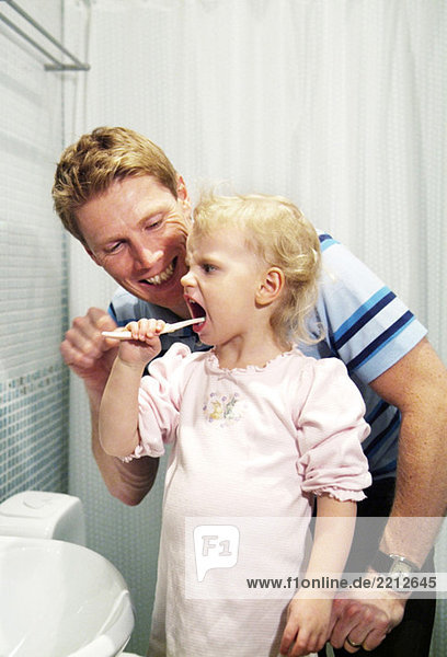 Dad helping daughter to brush her teeth