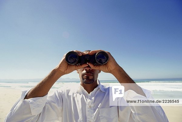Close-up of man looking through binoculars on beach
