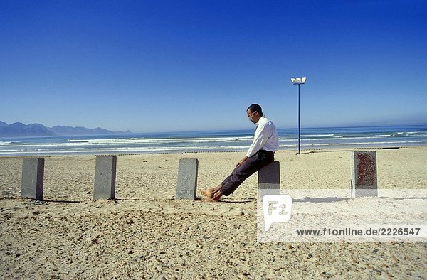 Seitenansicht Businessman sitting auf konkrete Pole-Position auf Strand