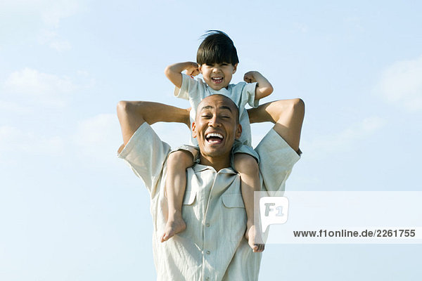 Man carrying son on shoulders  both smiling at camera