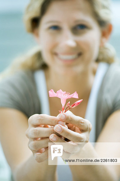 Woman holding flower in hands  smiling at camera  focus on foreground