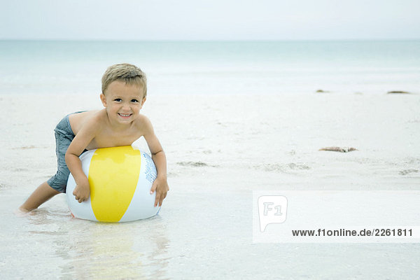 Kleiner Junge liegt auf dem Strandball am Strand und lächelt die Kamera an.