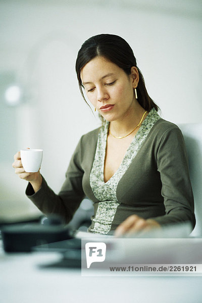 Frau am Schreibtisch sitzend  Kaffeetasse haltend  nach unten schauend