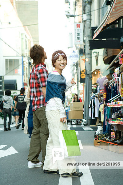 Junges Paar auf der Straße  Frau mit Einkaufstasche  lächelnd über die Schulter vor der Kamera