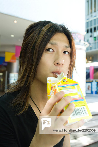 Young man drinking juice from a carton  looking away  close-up