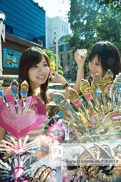 Zwei junge Frauen auf dem Straßenmarkt  probieren Haarschmuck an  lächeln
