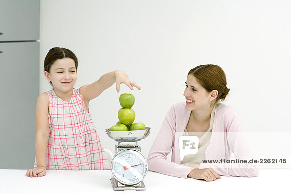Mutter und Tochter stapeln Äpfel  beide lächelnd.