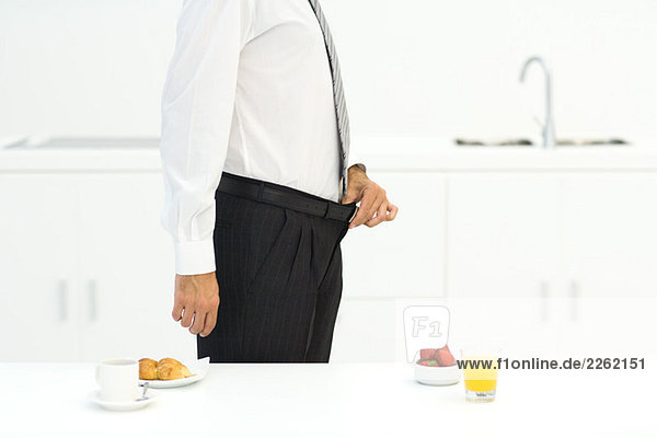 Mann steht in der Küche neben zwei Frühstücksmöglichkeiten  hält Hosenbund  beschnitten