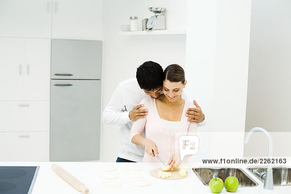 Paar steht zusammen in der Küche  Frau schneidet Äpfel  Mann lehnt Kopf auf der Schulter