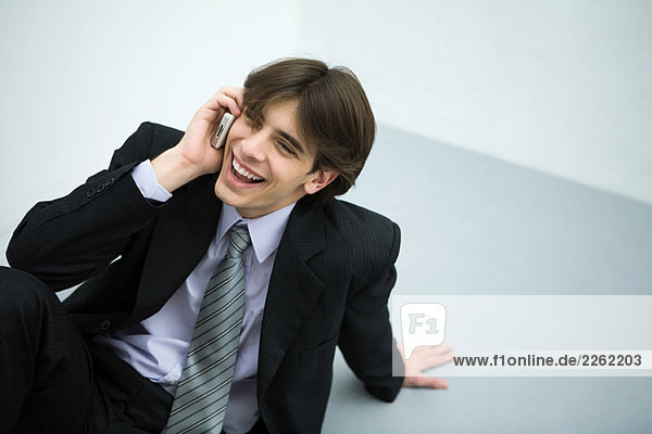 Young man in suit sitting on the ground  using cell phone  smiling
