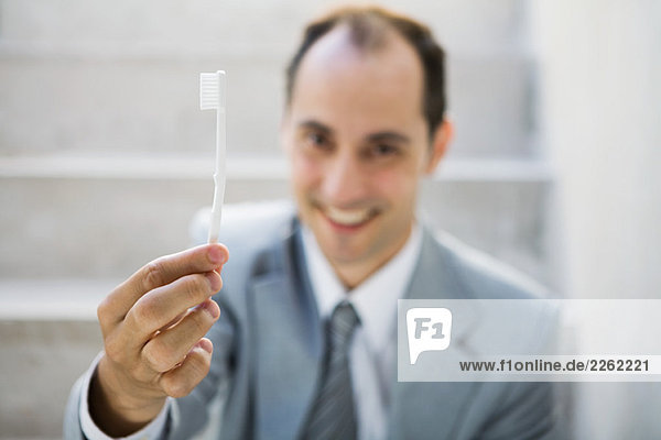 Geschäftsmann hält Zahnbürste hoch  lächelt in die Kamera  fokussiert auf den Vordergrund