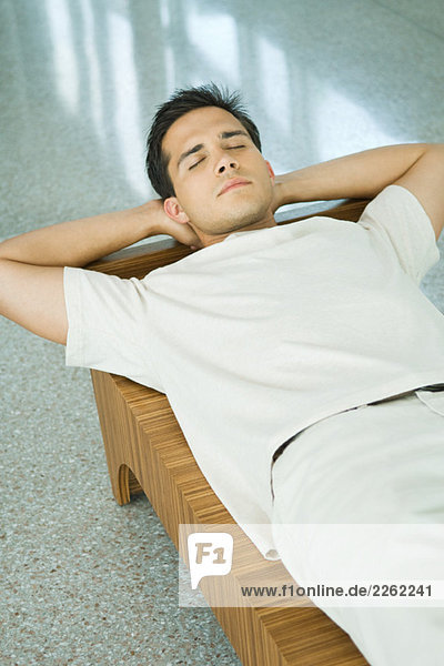 Young man lying on bench with hands behind head  eyes closed