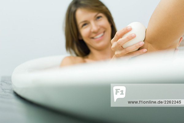Frau in der Badewanne sitzend  Bein mit Seife waschend  lächelnd