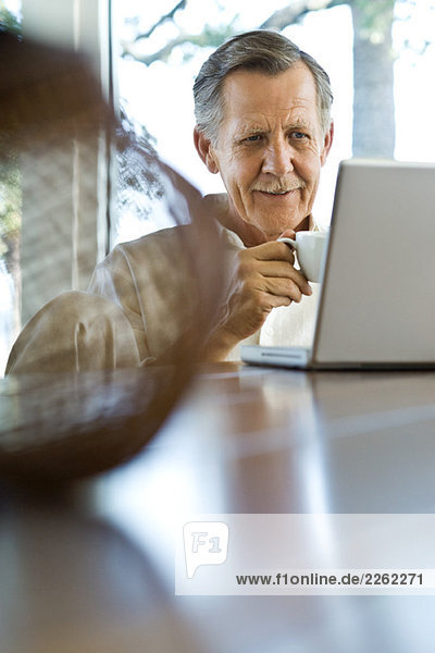 Senior Mann am Tisch sitzend  mit Laptop-Computer  Kaffeetasse haltend