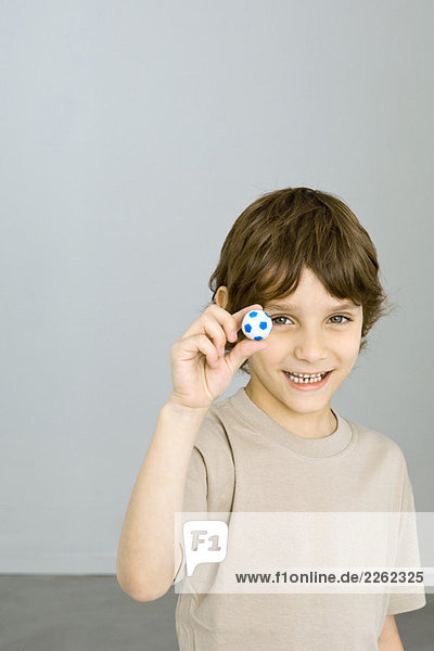 Kleiner Junge hält Miniatur-Fußball hoch  lächelt in die Kamera