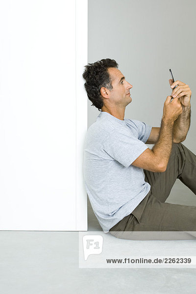 Mann sitzt auf dem Boden  schaut auf das Handy  Seitenansicht