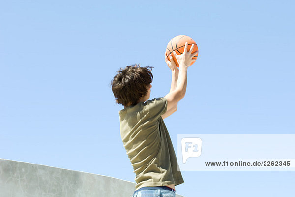 Teenager-Junge im Freien stehend  Basketball werfend  Blickwinkel niedrig
