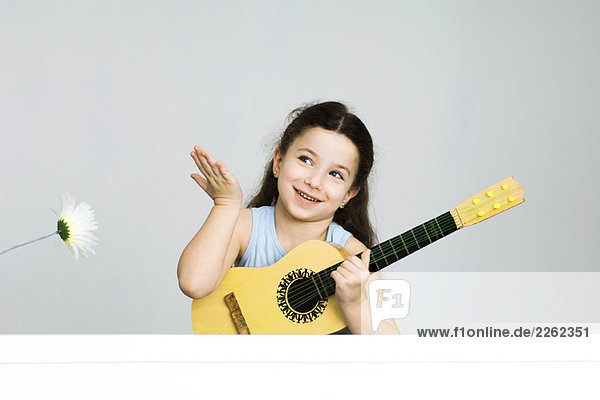 Kleines Mädchen hält Gitarre  Hand in Geste erhoben  lächelnd