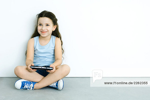 Kleines Mädchen sitzt auf dem Boden  spielt Handheld-Videospiel  lächelt