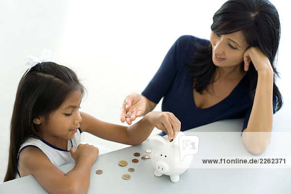 Mutter und Tochter legen Münzen im Sparschwein zusammen  Hochwinkelansicht