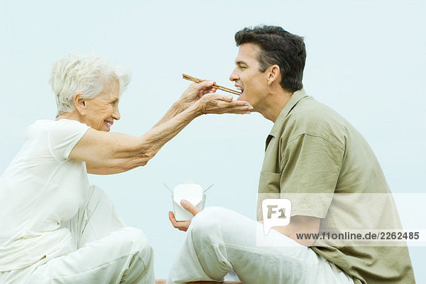 Seniorin füttert erwachsenen Sohn mit Essstäbchen  Seitenansicht