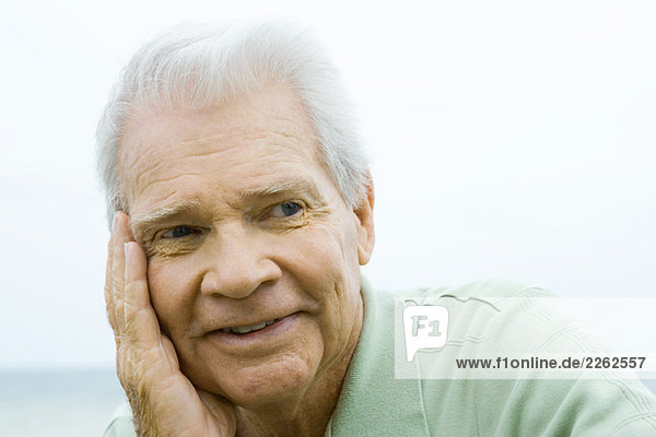 Senior man with hand on cheek  smiling  looking away