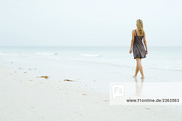 Frau im Sonnenkleid am Strand entlang  Rückansicht