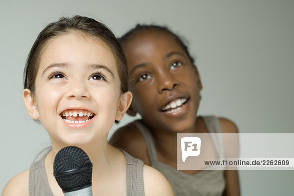 Zwei junge Mädchen  die zusammen ins Mikrofon singen  lächeln und aufschauen