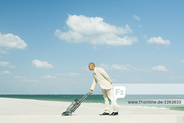 Man in suit using vacuum cleaner on beach  full length