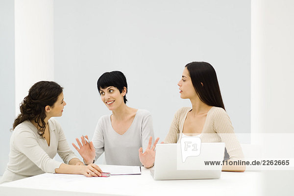 Three businesswomen sitting at table  having discussion  one gesturing with hands