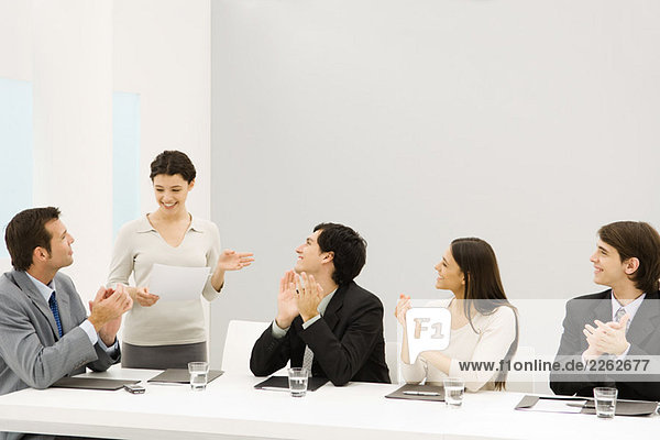 Businesswoman standing and speaking  seated colleagues clapping  smiling