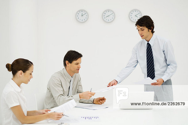 Businessman discussing document with colleagues  clocks on wall in background