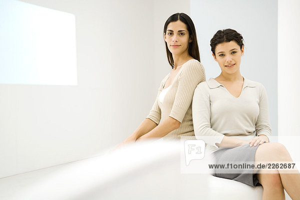 Weibliche Geschäftspartner sitzen zusammen und lächeln in die Kamera.