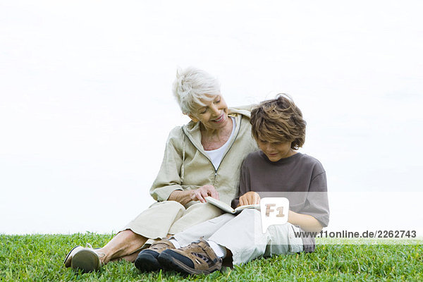 Großmutter und Enkel sitzen Seite an Seite auf dem Boden und lesen gemeinsam ein Buch.