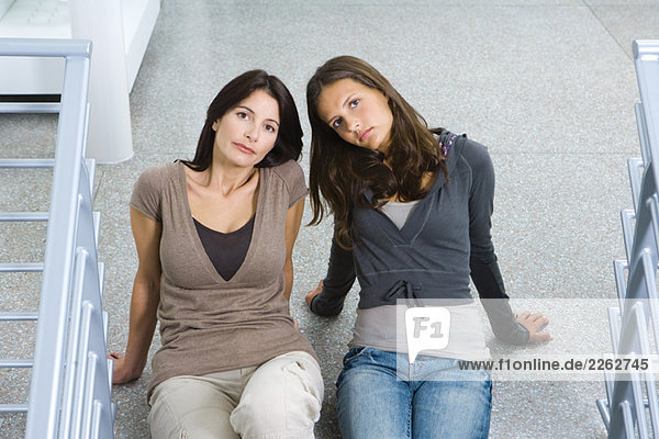 Mother and daughter sitting on the ground together  both looking up at camera