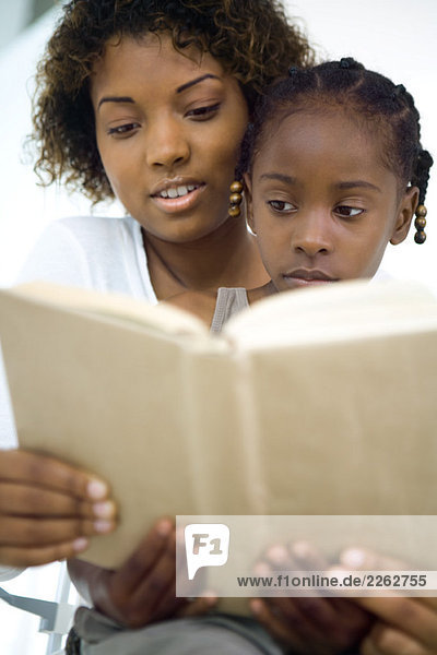Mutter und Tochter lesen gemeinsam Buch  Mädchen sitzt auf dem Schoß der Frau  Nahaufnahme