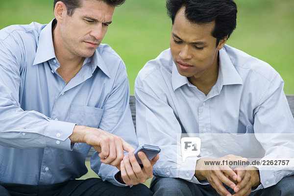 Zwei Geschäftsleute sitzen zusammen im Freien  beide schauen zusammen auf das Handy.
