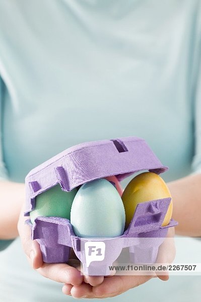 Frau hält Eierkarton mit bunten Ostereiern