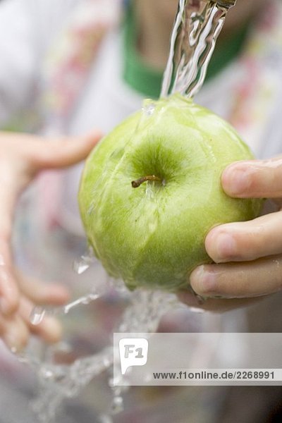 Kind hält grünen Apfel unter Wasserstrahl