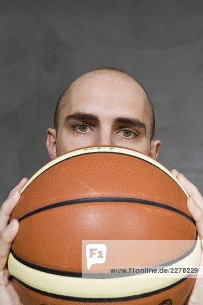 Ein junger Mann mit einem Basketball  der sein Gesicht teilweise verdeckt.
