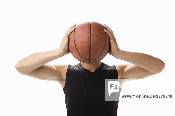 Ein Studioporträt eines jungen Mannes  der einen Basketball vor sich hält.